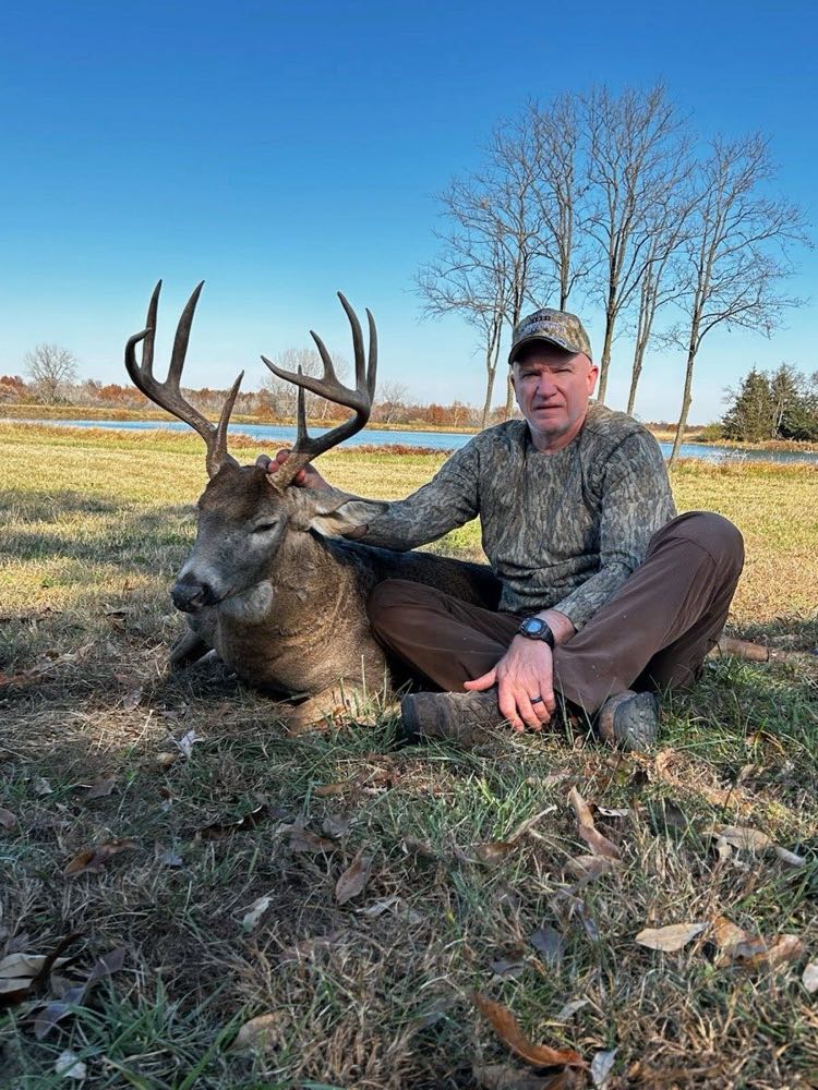 Hunter with a wide-racked Missouri whitetail buck in an open field by the water
